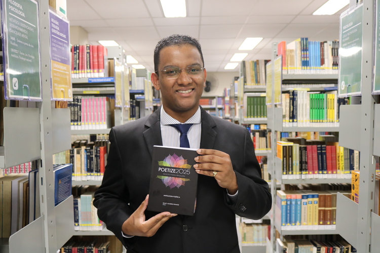 Alex Rodrigo, segurando o livro Poetize 2025 na Biblioteca do Assunção