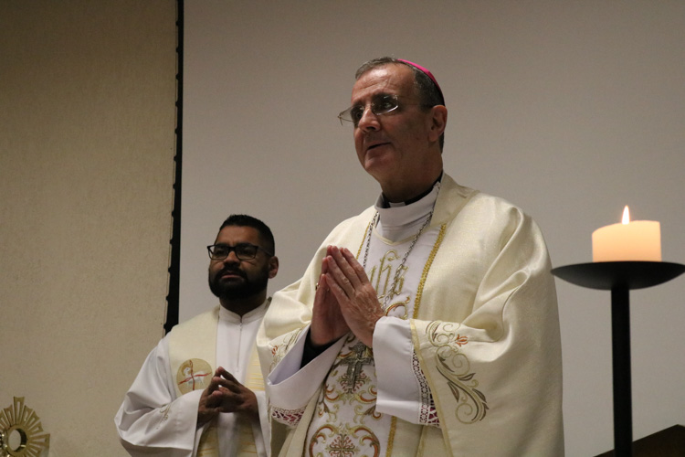 Dom Carlos com as mãos postas em oração, ao lado de outro sacerdote, em frente ao altar iluminado por velas.