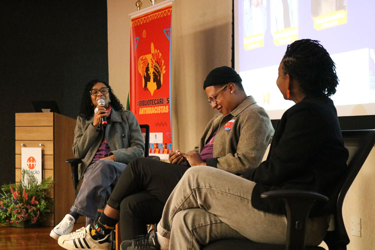 Prof.ª Carmem Lúcia, mediando palestra com palestrantes convidados Ueliton dos Santos e Raquel Gonçalves