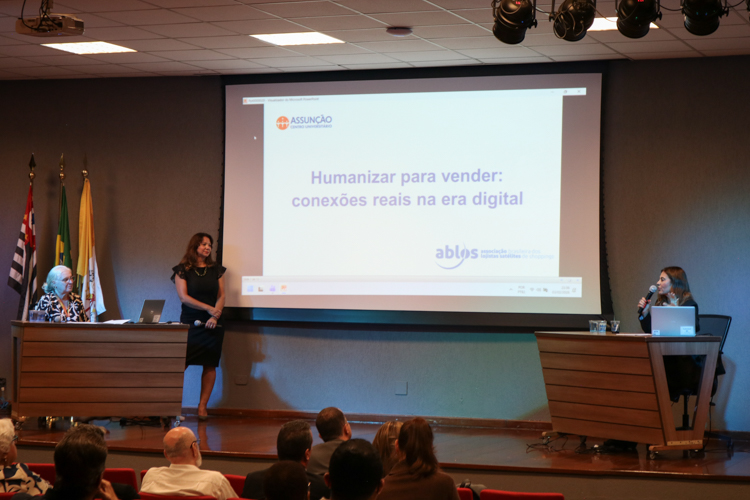 Palestrantes e mediadora no palco, durante debate.